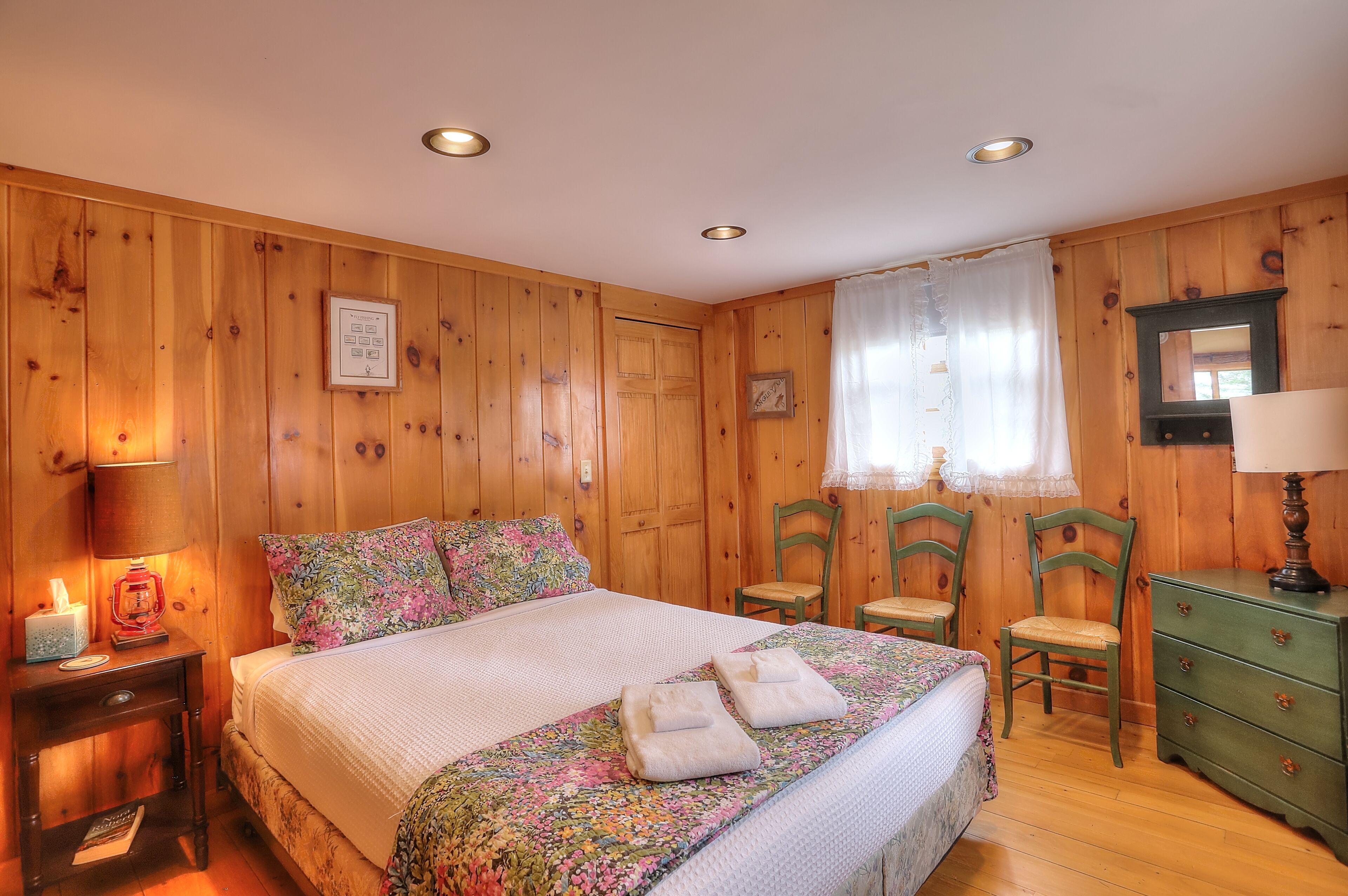 A wooden-paneled bedroom with a bed, two chairs, a dresser, and a nightstand.