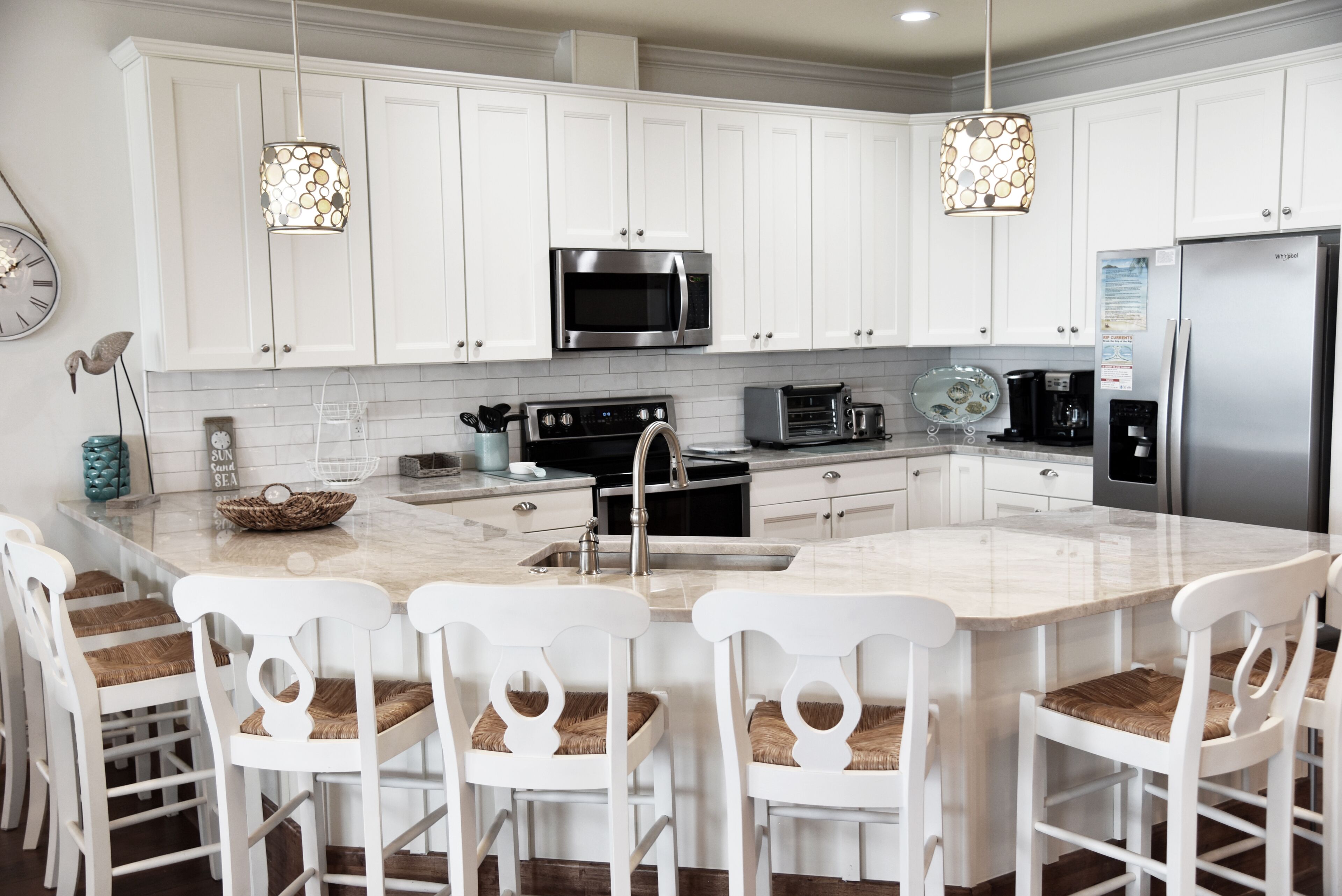 A modern kitchen with white cabinets, a central island with bar stools, stainless steel appliances, and pendant lighting.