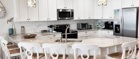 A modern kitchen with white cabinets, a central island with bar stools, stainless steel appliances, and pendant lighting.