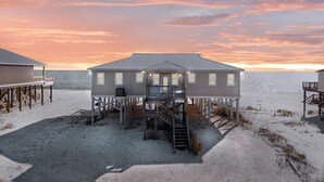 Et strandhus med metal tag, flere vinduer og en trappe op til en terrasse.