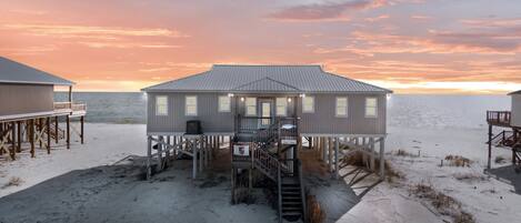A beach house with a metal roof, multiple windows, and a staircase leading to a deck.