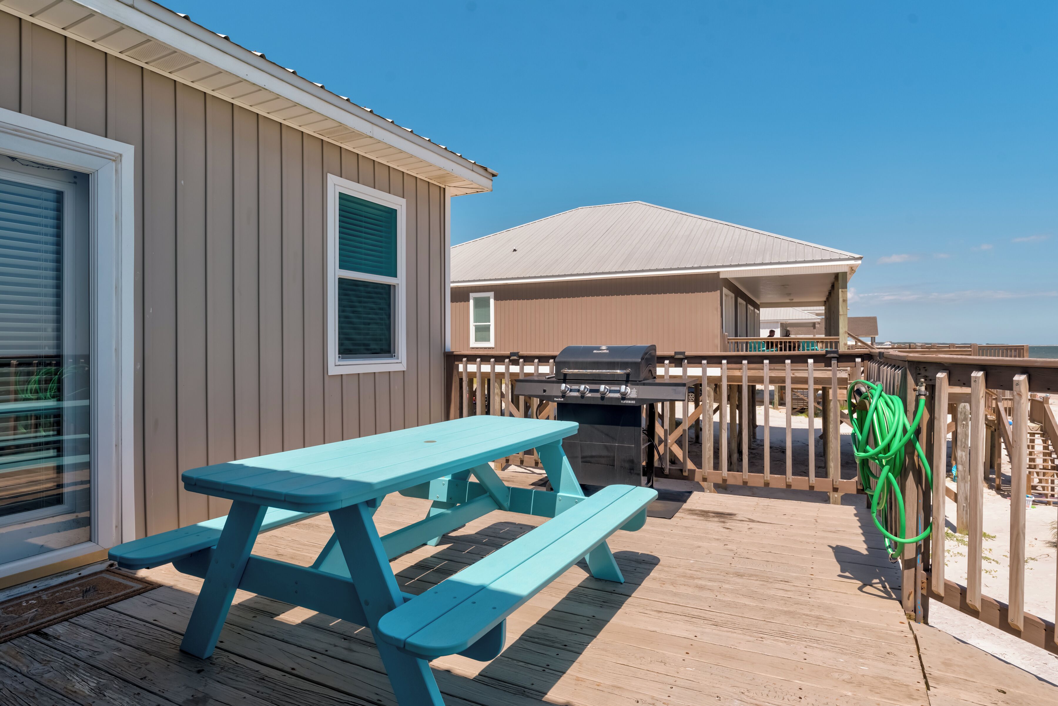 A wooden deck with a picnic table and a grill, overlooking a beach.