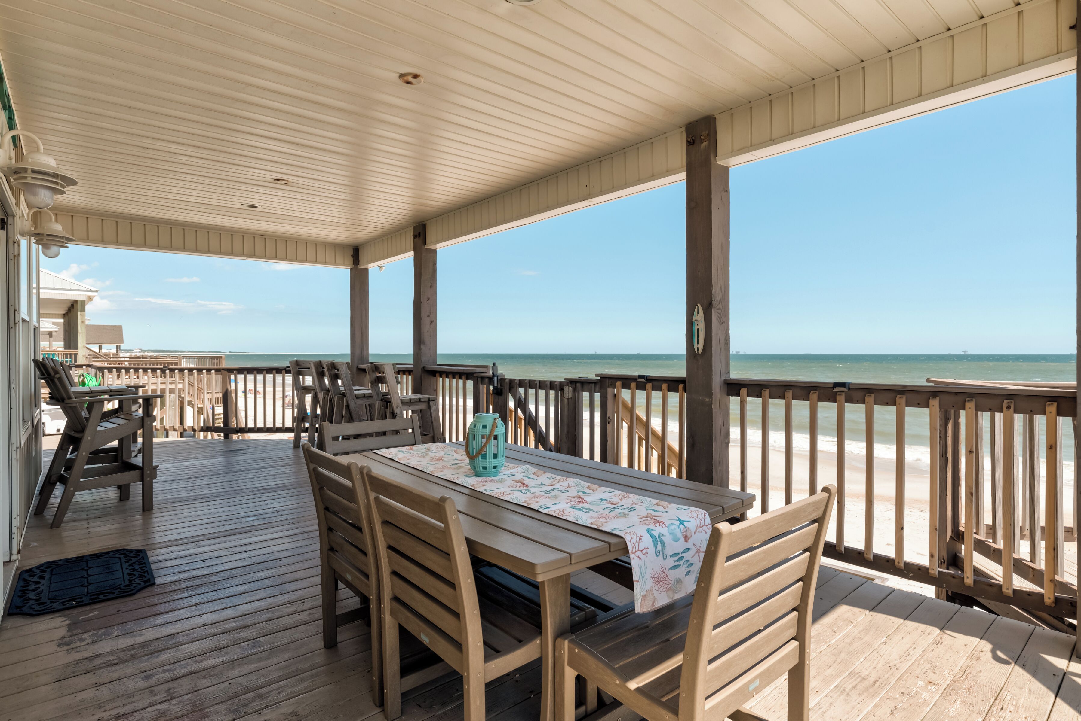 A wooden deck with a table and chairs, overlooking a beach.