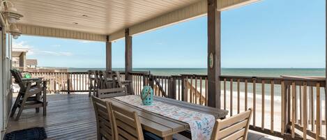A wooden deck with a table and chairs, overlooking a beach.