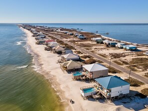 Luftaufnahme einer Küstenlandschaft mit Strandhäusern, einem Schwimmbad und einer Straße.
