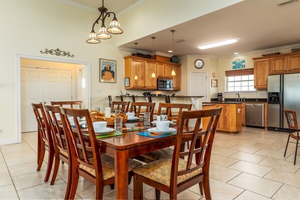 A spacious kitchen with wooden cabinets, a dining table set for six, and a refrigerator. - Thisldu | Christmas and NYE availability. Gulf Front (Dauphin Island)