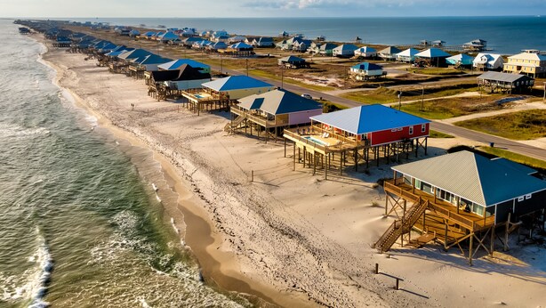 Una zona costera con casas sobre pilotes, una playa de arena y el océano.
