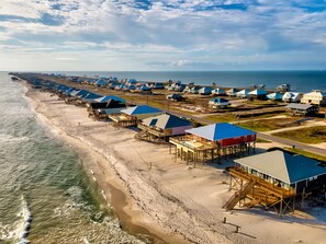 A coastal area with beach houses on stilts, a sandy beach, and the ocean. - At Last | Beach Front. Book your summer get-away today (Dauphin Island)
