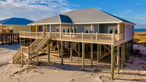 Una casa de playa con un balcón y una escalera que conduce al nivel superior.