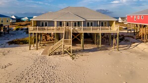 Una casa frente a la playa con un porche de madera y una escalera que lleva a la entrada.