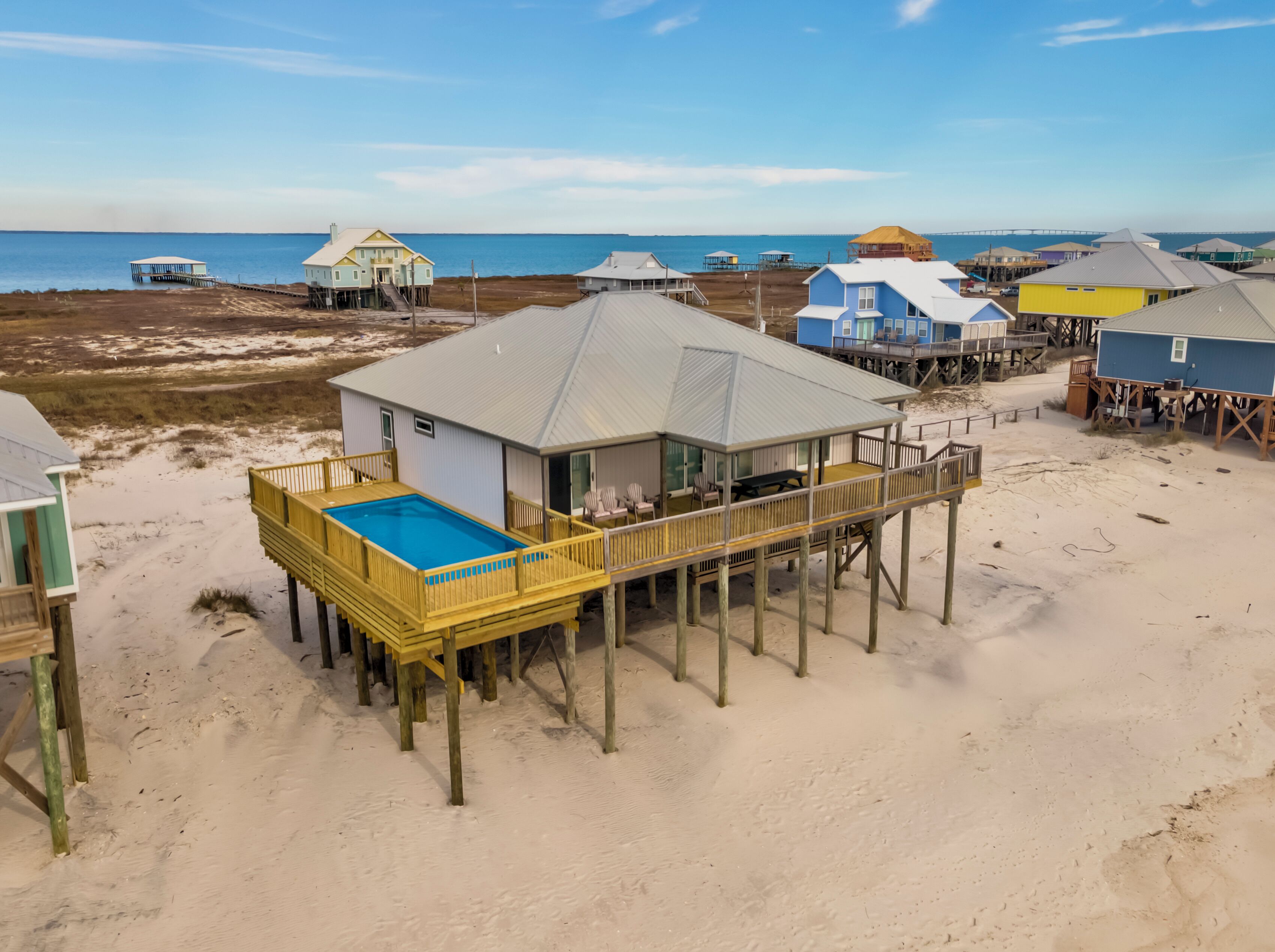 A beach house with a pool on a wooden deck, surrounded by other beach houses.