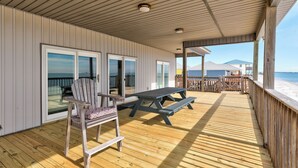 A covered deck with a wooden bench and a chair, a picnic table, and a view of the beach and mountains in the background. - Salty Piece of Land | Nightly openings 8/22. Pool. (Dauphin Island)