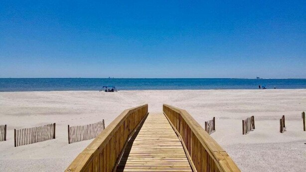 A wooden boardwalk leading to a beach with a clear blue sky.
