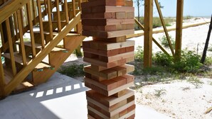 A stack of wooden planks outdoors with a wooden staircase in the background.