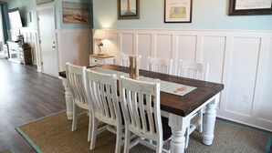 A dining area with a wooden table and white chairs, a lamp, and framed artwork on the walls.