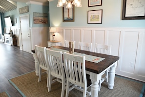A dining area with a wooden table and white chairs, a lamp, and framed artwork on the walls.