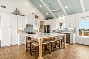 Una cocina amplia con armarios blancos, una isla grande con taburetes, un ventilador de techo y vistas a través de una ventana.
