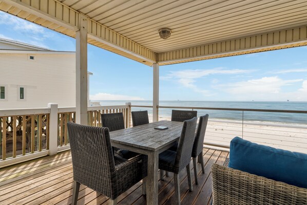 Terraza techada al aire libre con una mesa y sillas, con vista a la playa.