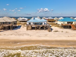 A beachfront property with multiple wooden structures elevated on stilts, featuring outdoor seating areas and a view of the ocean.