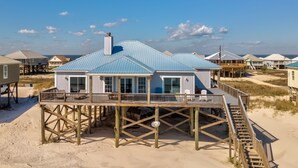 Ein Strandhaus mit einer Holzterrasse und einer Treppe, die zu einer zweiten Ebene führt.