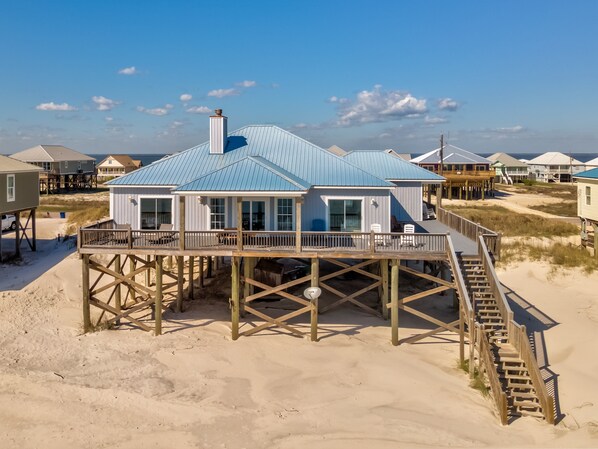 A beach house with a wooden deck and a staircase leading to a second level.