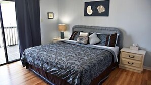 Un dormitorio con cama, mesita de noche, lámpara y un cuadro en la pared.