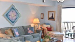 Una sala de estar con un sofá gris, una mesa de centro de vidrio y un balcón con una silla.