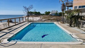 Piscina rectangular con agua cristalina azul, rodeada por una terraza de madera y una valla de metal.