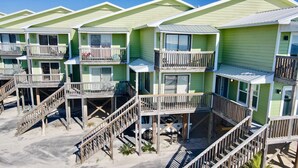 Una hilera de casas de playa de varios pisos, con balcones de madera y un primer piso de arena.