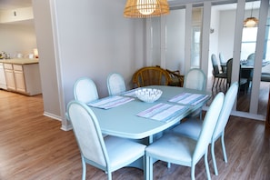 A dining area with a light blue table and matching chairs, a woven light fixture, and a view into the kitchen.