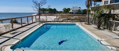 A rectangular pool with clear blue water, surrounded by a wooden deck and a metal fence.