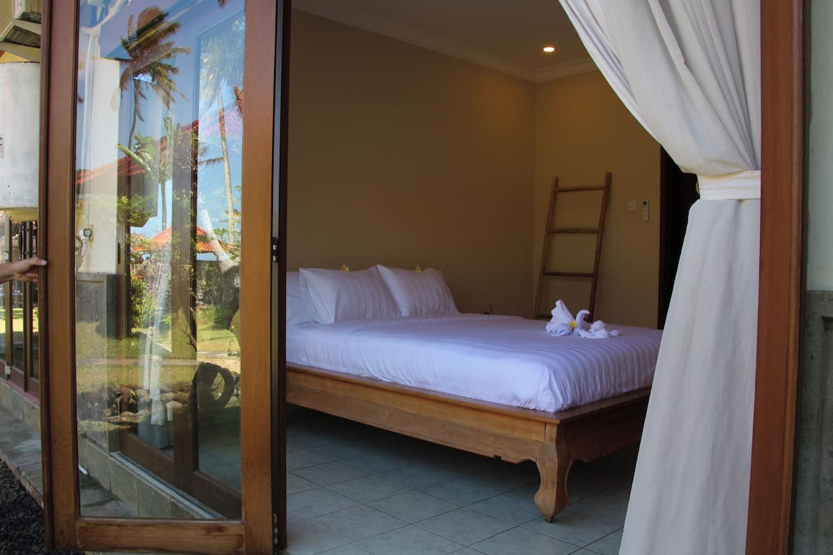 A bedroom with a wooden bed, a glass door leading to a balcony, and a view of palm trees.
