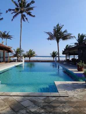 A swimming pool with clear blue water, surrounded by palm trees and a view of the ocean. - Bali Hai Island Resort (Pekutatan)