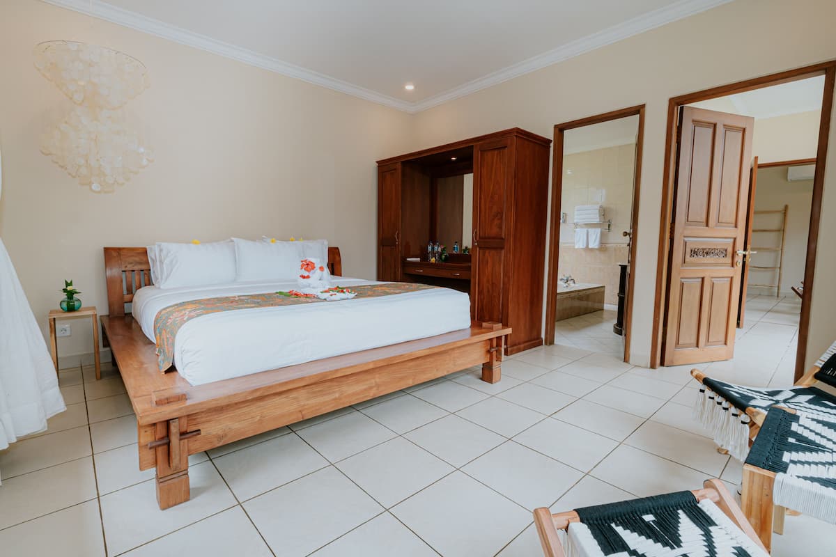 A spacious bedroom with a large bed, wooden wardrobe, and a bathroom visible through an open door.