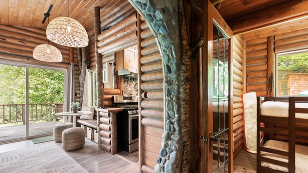 Interior de una cabaña de troncos con comedor, cocina y zona de descanso con literas.