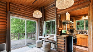 Interior de una cabaña de troncos con comedor, cocina y grandes puertas corredizas que dan a una terraza.