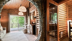 Interior de una cabaña de troncos con un gran arco de piedra, pisos de madera, un sofá, una mesa de comedor y vistas al exterior.