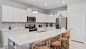 A modern kitchen with white cabinets, stainless steel appliances, a large island with a sink, and two pendant lights.