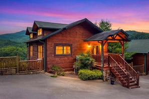 A wooden cabin with a porch and staircase, surrounded by a stone wall and a view of the forest. - Lovin' the View - Gorgeous views plus a true cabin feel! (Gatlinburg)