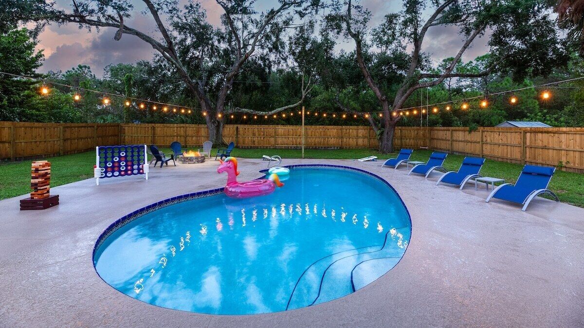 A backyard with a swimming pool, lounge chairs, a flamingo float, and a game table.