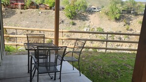 Une terrasse extérieure avec une table et des chaises, offrant une vue sur un paysage vallonné à la végétation clairsemée, avec quelques bâtiments visibles au loin.