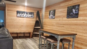 Une pièce aux murs lambrissés, avec une table à manger et des bancs, un ventilateur de plafond et des œuvres d’art accrochées aux murs.