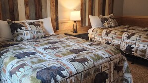 Une chambre d’hôtel avec deux lits, chacun recouvert d’une courtepointe matelassée ornée de motifs animaliers. Il y a une table de chevet avec une lampe entre les deux lits, et les murs sont recouverts de panneaux en bois.