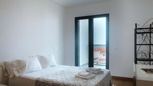 Ein Schlafzimmer mit einem Bett, einer Balkontür und einem Metallregal.