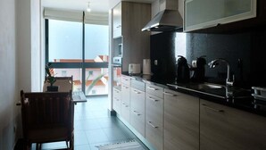 Eine moderne Küche mit schwarzem Arbeitsplatz, Spüle aus Edelstahl und Holzausstattung. Ein Stuhl und ein Blumentopf stehen in der Ecke.