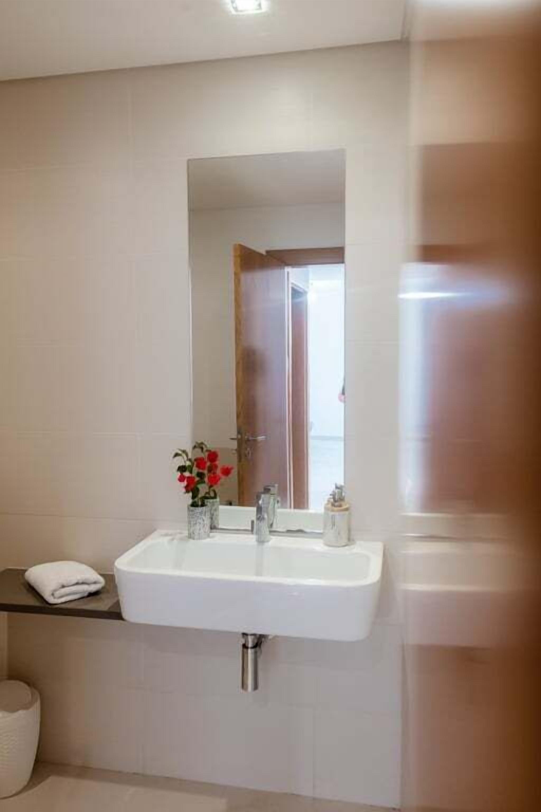 Een badkamer met een witte wastafel, een spiegel en een kleine vaas met rode bloemen.