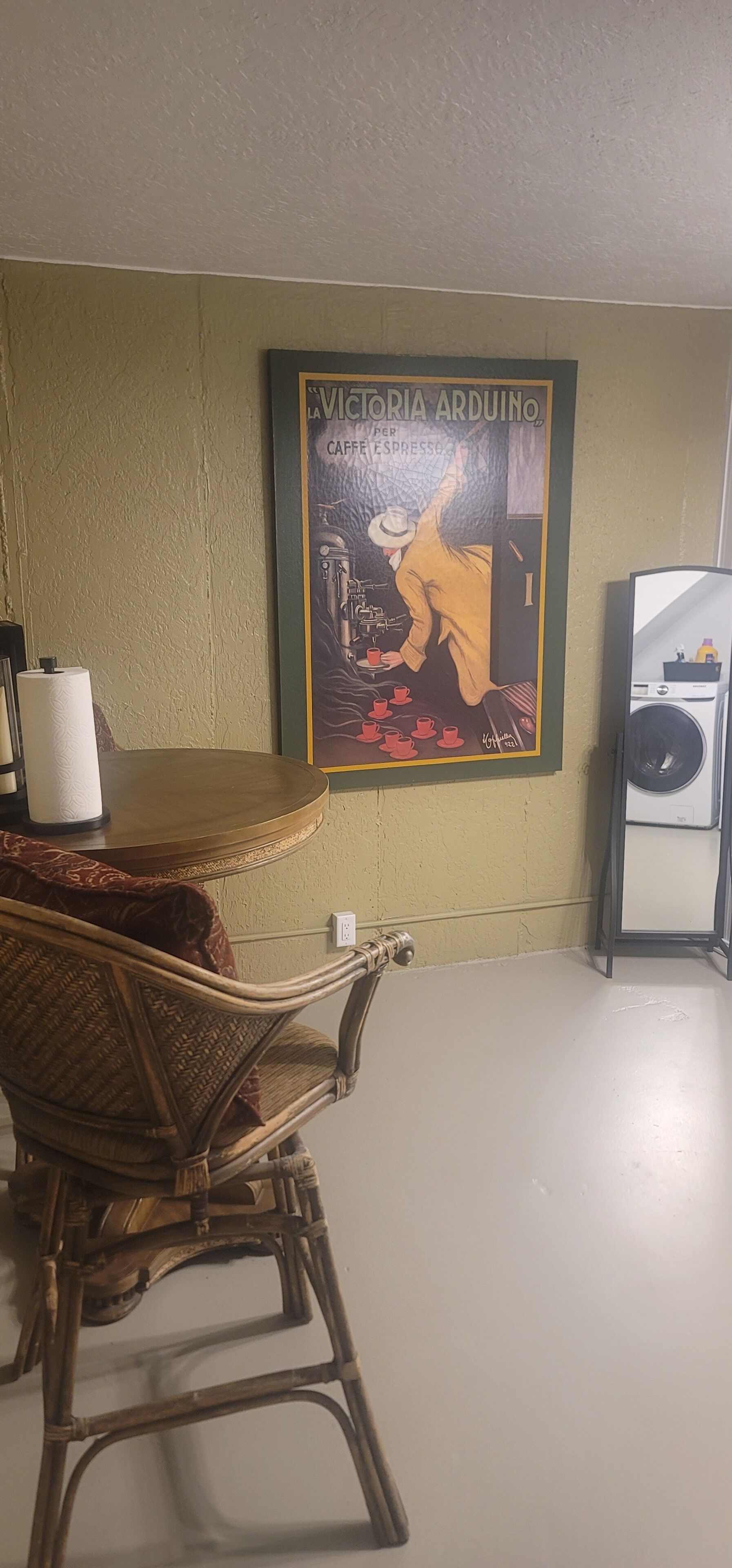 A room with a wicker chair, a poster on the wall, and a washing machine.