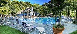 Ein Swimmingpool mit Liegestühlen und Sonnenschirmen, umgeben von Bäumen und einem Gebäude mit einem geneigten Dach.