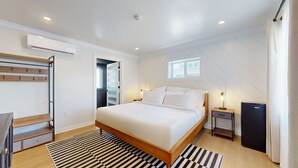 Un dormitorio con cama, mesita de noche, escritorio, silla, perchero y aire acondicionado.