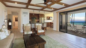 Un'ampia zona giorno con soffitto in legno, un'area pranzo con sedie in vimini e un balcone vista oceano.